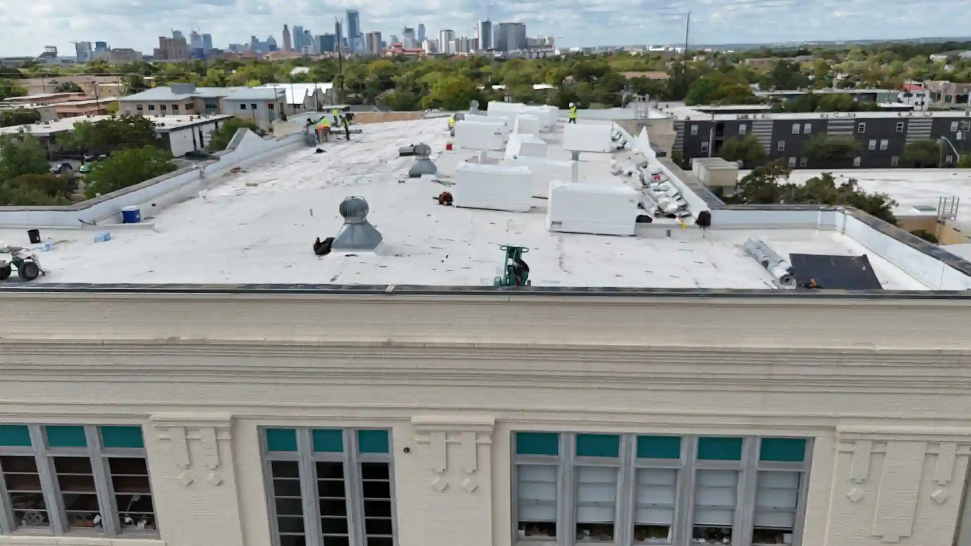 "Aerial view of a commercial building with a white flat roof and workers on-site