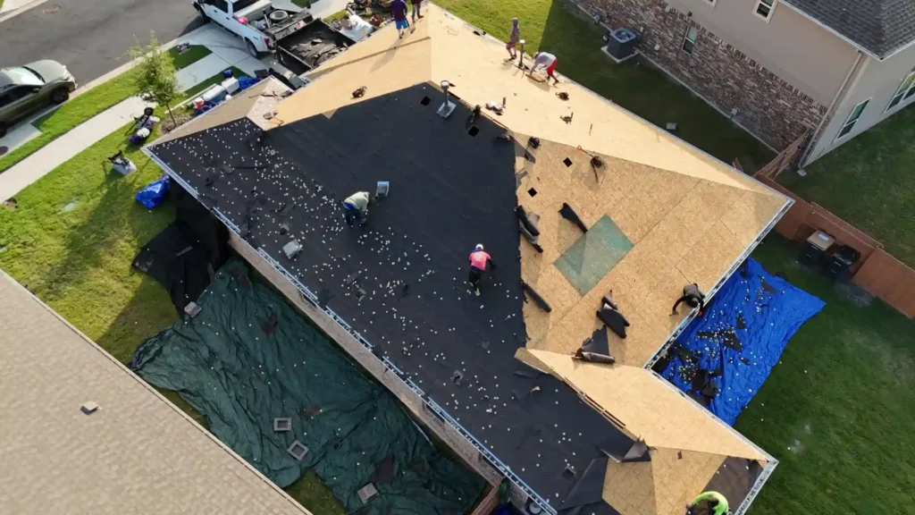 Roofers install black underlayment on stripped roof decking