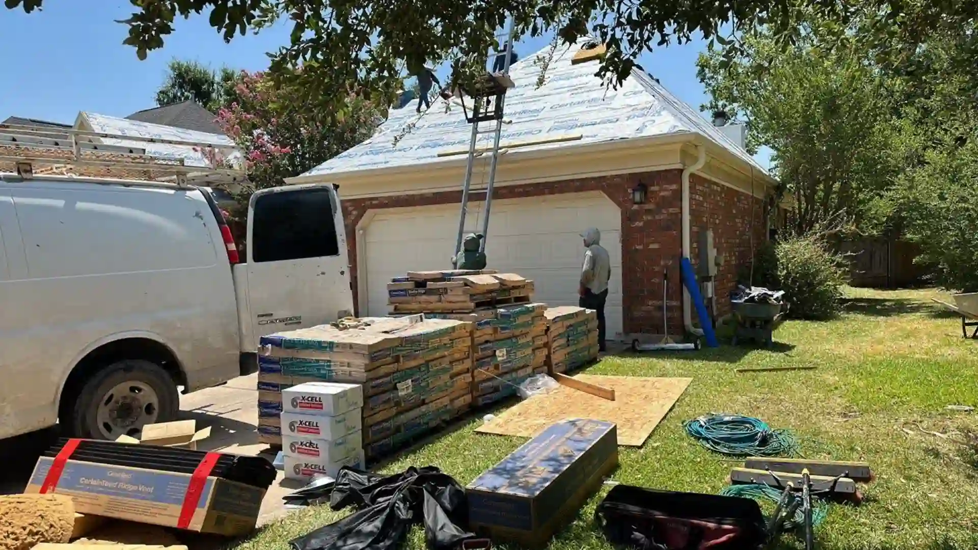 Roofing materials stacked with a ladder and worker on site.