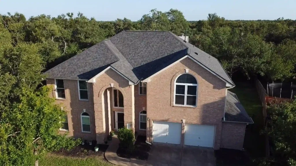 Two-story brick house with a dark shingle roof surrounded by trees.