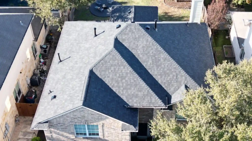 Aerial view of a brick house with a dark gray shingle roof.