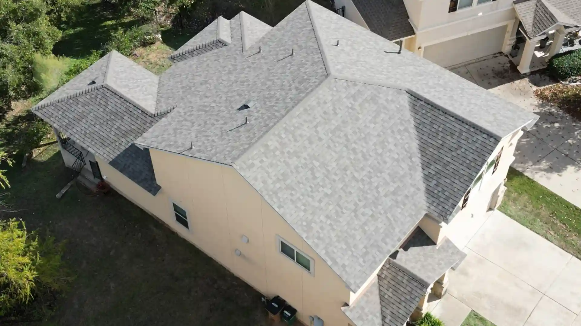 Aerial view of a beige house with a light gray shingle roof