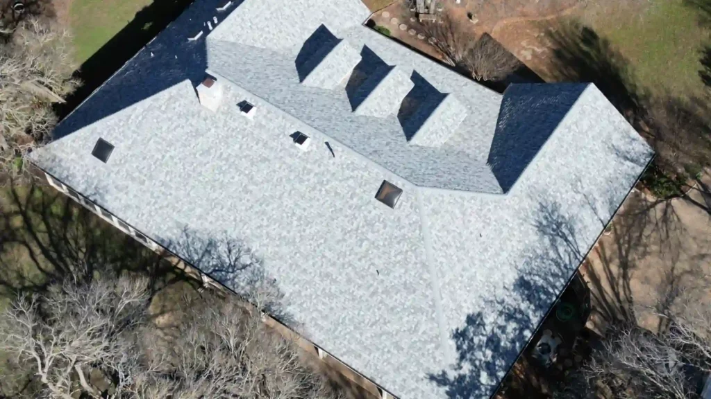 Aerial view of a large house with a light-colored shingle roof and dormer vents.