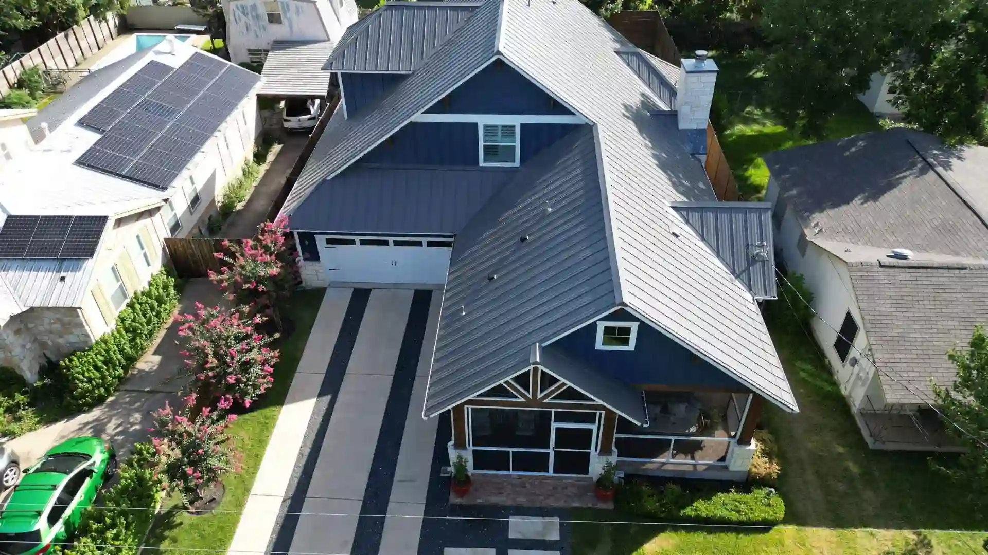 Aerial view of a blue house with a gray metal roof and modern driveway.
