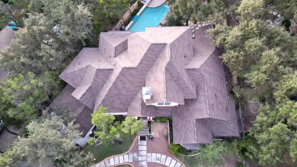 Aerial view of a large house with a brown shingle roof and backyard pool.
