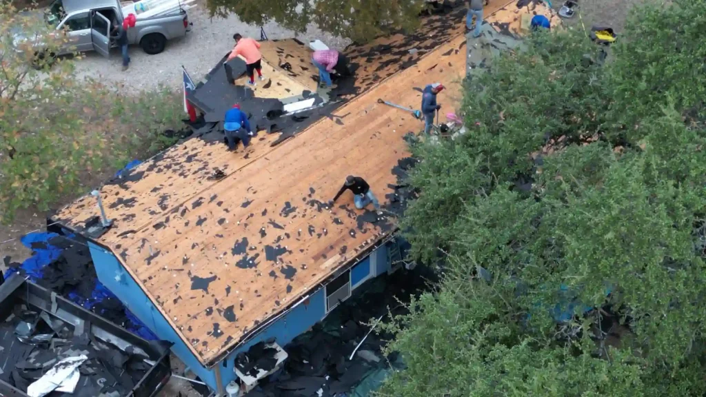 Workers tearing off old shingles during roof replacement.