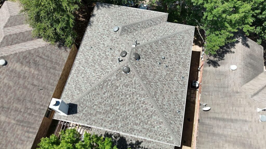 Aerial overhead photo of a complex residential home featuring a newly installed weathered wood shingle roof replacement with roof vents and chimney flashing in Austin, TX.